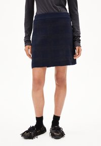 Kniebundrock aus navyblauem Strick mit einem strukturierten Karomuster, ausgestattet mit einem breiten Bund und geradem Schnitt, kombiniert mit schwarzen Fransen-Schuhen und Socken.