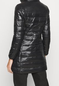 Abrigo acolchado negro con un acabado brillante. Presenta un cuello alto y mangas largas, con costuras horizontales en todo el cuerpo.