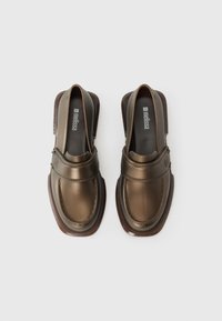 Brown synthetic slip-on shoes with a glossy finish, rounded toe, and contrasting darker outsole. Features a front strap and visible stitching.