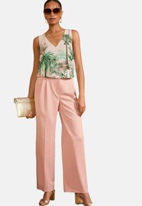 Light pink wide-leg trousers paired with a sleeveless v-neck top featuring green palm leaf prints. Accessories include a gold clutch and sunglasses.