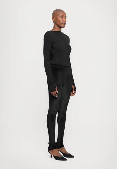 Black long-sleeve top paired with black velvet leggings and black pointed-toe heels, showcasing a sleek and fitted silhouette.