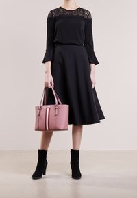 Schwarzes Kleid mit Spitzendetails, rosafarbene Lederhandtasche mit vertikalen Streifen, schwarze Ankle-Boots mit hohem Absatz. Glatte Texturen, klassisches Design.