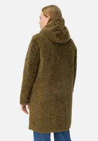 Olijfgroene, donzige jas met een capuchon, met een zachte, gestructureerde oppervlakte en een losse pasvorm. De jas reikt tot halverwege het bovenbeen.