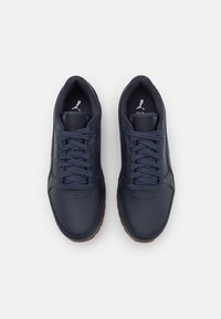 Mörkblå lädersneakers med kontrasterande brun gummisula, med texturerade detaljer, snörningsdesign och logotyp på tungan.