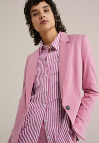 Růžový blazer přes růžovou a bílou pruhovanou košili s knoflíky. Blazer má klopové límce a zapínání na knoflík. Hladký materiál.