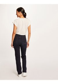 Donkerblauwe jeans met een slanke pasvorm en achterzakken, gecombineerd met een lichtbeige T-shirt met korte mouwen. Witte sneakers maken de outfit af.
