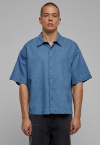 Kratka majica s kratkimi rokavi v svetlom modrem denimu, s klasičnim ovratnikom, šestimi gumbi in sprostitvenim krojem.