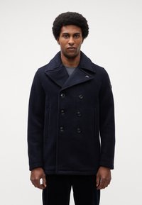 Marineblaue Wollpeacoat mit doppelter Knopfleiste, großen Revers, zwei Fronttaschen und schwarzen Knöpfen. Texturiertes Material, warmes Design.