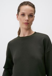 Donkergroen sweatshirt met een ronde hals en een losse pasvorm. Zachte textuur en lange mouwen, benadrukken een casual ontwerp.