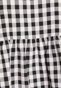 Tissu à carreaux noir et blanc avec une surface texturée. Présente un détail plissé le long de l'ourlet ainsi que des rayures alternées épaisses et fines.