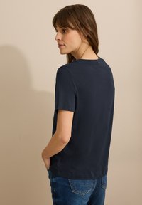 Camiseta de manga corta color azul marino, con cuello redondo, de suave tela de algodón. Combinada con jeans de mezclilla claros. Diseño simple, sin patrones o acentos visibles.