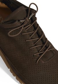 Chaussure en cuir perforé marron avec bout rond, dotée de lacets assortis et d'une semelle en caoutchouc épaisse. Finition avec des coutures discrètes.