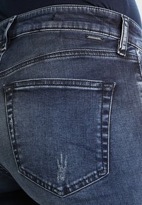 Blauwe spijkerbroek met een achterzak met een subtiele vervaagde print, contrasterende stiksels en een klein metalen logo nabij de tailleband.