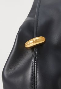 Melnā ādas soma ar izteiktu zelta aparatūru, uz kuras ir iegravēts "FURLA". Gluda tekstūra ar redzamām šuvju detaļām.