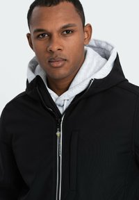 Veste zippée noire avec capuche, dotée d'une doublure intérieure grise. Comprend une poche poitrine et un détail en tissu texturé le long des coutures.