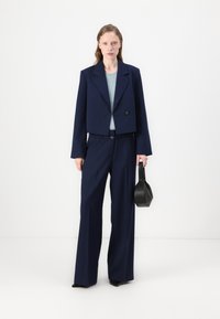 Navy blå cropped blazer med to knapper og vide bukser. Teksturert lyseblå topp under, sammen med en liten svart veske.
