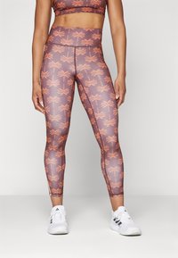 Läggings i ett lila tyg med ett mönster av orange palmträd. Hög midja med en mjuk textur, designad för träning.