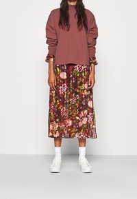 Felpa bordeaux con spalle scese indossata sopra un abito midi plissettato con fantasia floreale nei toni del bordeaux, rosa e verde. Sneakers bianche.
