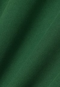 Close-up van groen textiel met een subtiel geweven patroon en zachte plooien die schaduwen creëren.