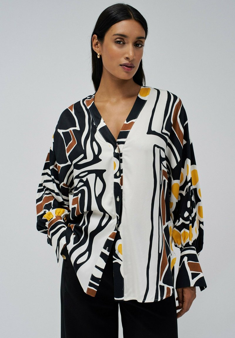 Chemise boutonnée avec un motif abstrait noir, blanc et beige, rehaussé d'accents jaunes et de manches plissées. Tissu lisse et léger.