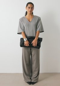 Pilkas per didelis V formos kaklo užsegimas, platūs pilki kelnės ir juoda pynimo rankinė. Sidabrinis apyrankė akcentuoja išvaizdą.