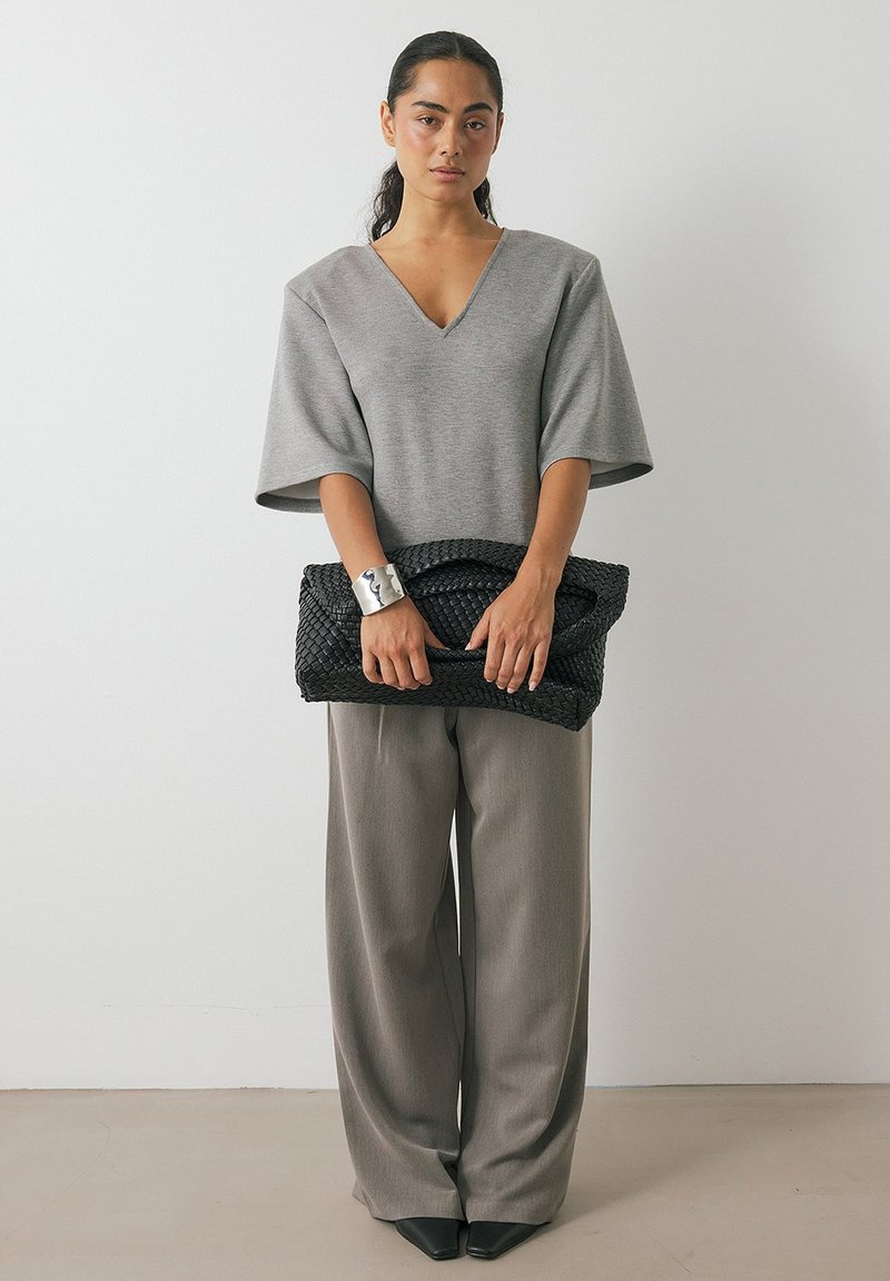 Pilkas per didelis V formos kaklo užsegimas, platūs pilki kelnės ir juoda pynimo rankinė. Sidabrinis apyrankė akcentuoja išvaizdą.