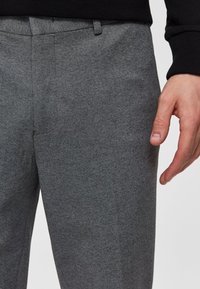 Pantaloni in lana grigia con una texture liscia, caratterizzati da una parte frontale piatta, passanti per cintura e tasche laterali, che mostrano un design sartoriale.