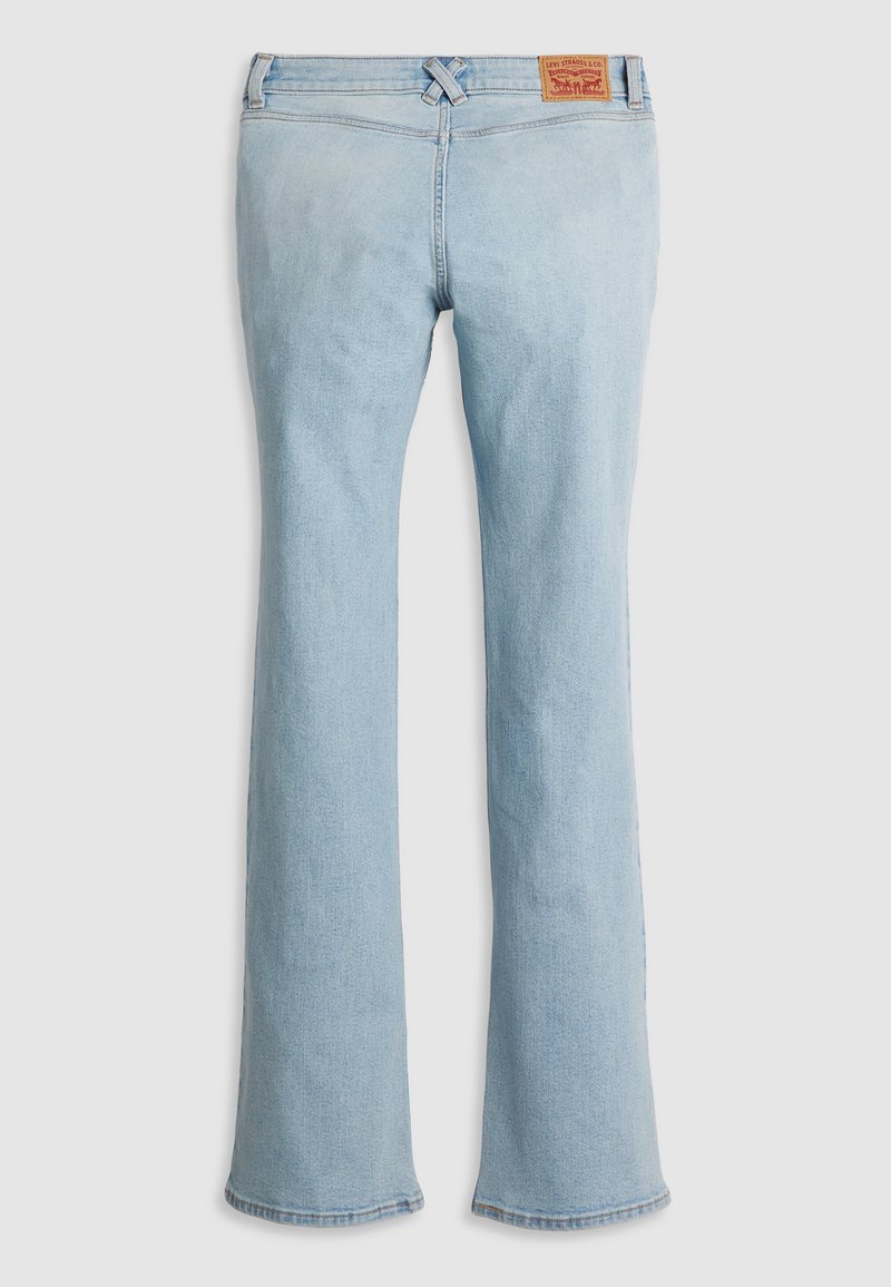 Jean en denim bleu clair évasé avec un design classique à cinq poches, fermeture à bouton à l'avant, et une patch en cuir beige sur la ceinture.