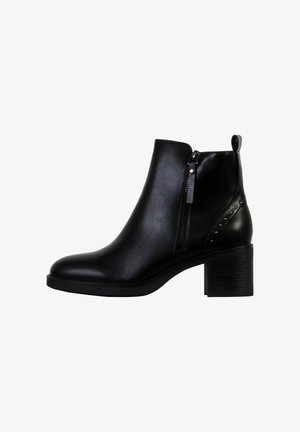 Bottine noire en simili cuir. Présente une fermeture éclair sur le côté, un bout rond, un talon carré et des détails cloutés au niveau de la cheville.
