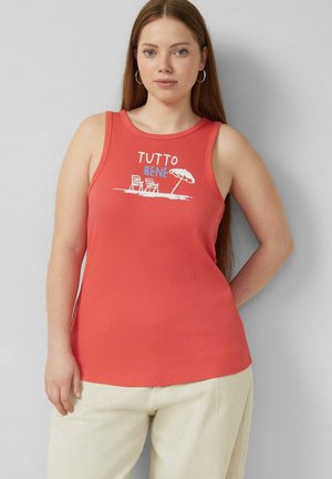 Jeune femme aux longs cheveux portant un top sans manches corail avec le texte "Tutto Bene" et un motif de chaise de plage et parasol, associé à un pantalon clair.