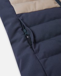 Izolowana kurtka z granatowymi i beżowymi panelami, kieszenią na zamek błyskawiczny, gładką teksturą tkaniny oraz pikowanym wyglądem dla lepszego ciepła.