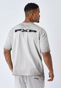 Camiseta de manga corta gris claro con cuello redondo, que presenta un logo negro "PXP" impreso en la parte posterior y una textura de algodón suave.