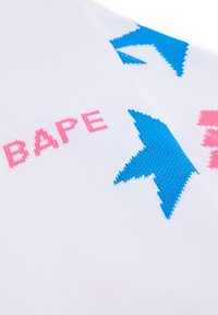 Weißer Stoff mit rosa und blauen gestrickten Grafiken, darunter das Wort "BAPE" und Sternformen. Glatte Textur mit lebendigen Farben.