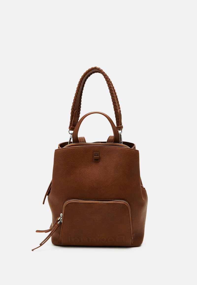 Mochila de cuero marrón con asa trenzada en la parte superior, bolsillo frontal con cremallera, acabado texturizado y logo incrustado en el panel frontal inferior.