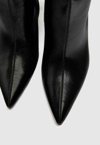 Botas de cuero negro hasta el tobillo con un diseño de punta afilada, textura suave y sutiles detalles de costura a lo largo de las costuras.