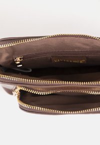 Cartera de cuero marrón con dos cremalleras doradas abierta, mostrando un interior de tela y un pequeño bolsillo con cremallera en el interior.