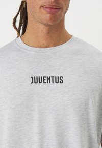 Svetlo šedé bavlnené tričko s okrúhlym výstrihom a čiernym logom "JUVENTUS" potlačeným na hrudi. Mäkkučký, hladký povrch.