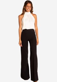 Haut à bretelles blanc avec un design drapé et un col haut, associé à un pantalon noir évasé taille haute. Texture lisse, détails minimalistes.