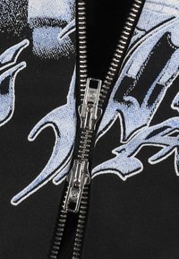 Czarna bluza z zamkiem błyskawicznym, wyróżniająca się wyraźnym jasnoniebieskim wzorem, teksturowanym materiałem oraz srebrnym metalowym zamkiem z przodu.