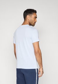 Gaiši zilas krāsas īsām piedurknēm T-krekls ar apaļu kakla izgriezumu, gludu tekstūru, vienkāršu dizainu un nelielu zīmola logotipu pie apakšmalas.