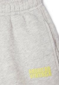 Pelēki sporta bikses, kas izgatavotas no mīksta, strukturēta auduma, ar elastīgu jostu un dzeltenu izšuvumu "AMERICAN VINTAGE" sānos.