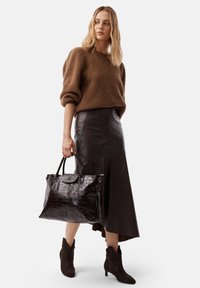 Maglione di lana marrone, gonna in pelle nera, borsa in pelle con stampa coccodrillo marrone scuro con manici e stivaletti in suede marrone con tacco.