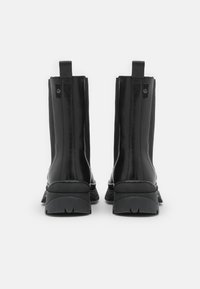 Černé kotníkové boty s hladkým a jemným syntetickým svrškem. Mají masivní podrážku a poutka na zadní straně pro snadné obouvání.