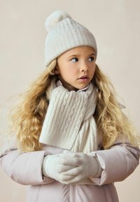 Gorro de punto crema con pom-pom, bufanda de canalé a juego y guantes. Abrigo aislante de color rosa pálido con cremallera, tela texturizada y suave brillo.