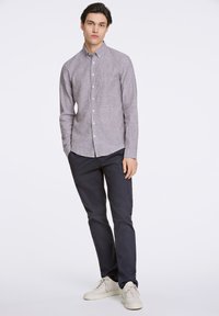 Camisa gris de botón con una textura sutil, combinada con pantalones oscuros de color navy y zapatillas de color claro. La camisa tiene un corte relajado y cuello.