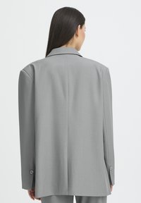 Grå oversized blazer med en glat tekstur, indsnippede revers og knappede manchetter; har et elegant, lige snit bagpå.