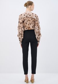 Flowy, patterned blouse with spotted beige and brown design, featuring ruffled sleeves, paired with slim black pants and tan block heels.