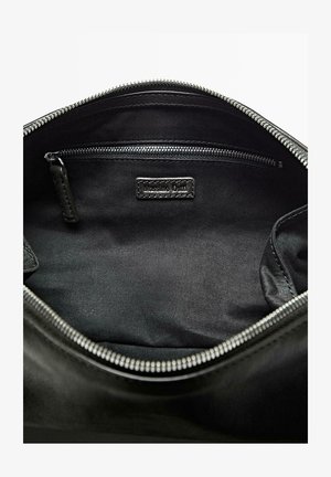 Intérieur d'un sac en cuir noir avec une texture lisse, comportant une poche zippée et une étiquette. Agrémenté de détails de fermeture éclair argentés.