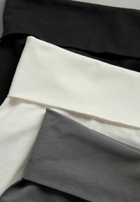 Három pár leggings fekete, fehér és szürke színben, puha, széles derékpánttal és sima, nem texturált felülettel.