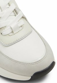 Sneaker in pelle bianca con dettagli grigi, punta tonda, linguetta imbottita e lacci bianchi. Superficie texturizzata con cuciture a contrasto e suola nera.